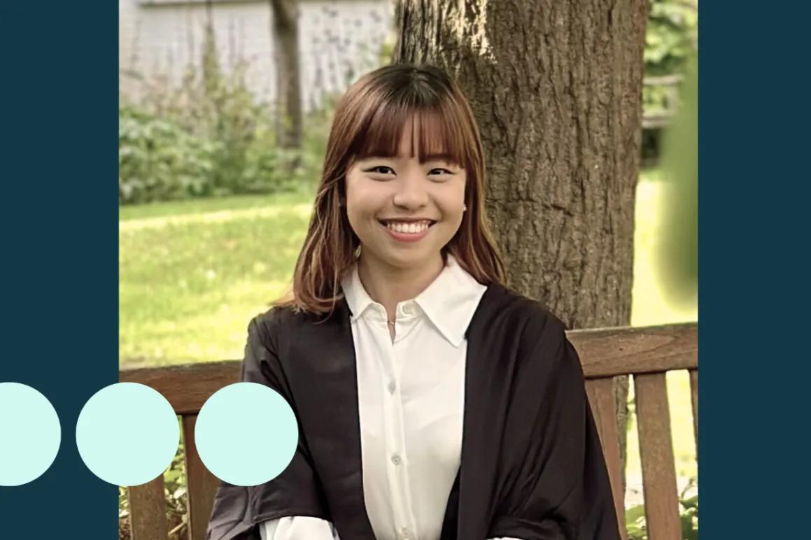Asian woman sat on bench in graduation gown