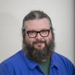 Headshot of a smiling bearded man wearing a blue shirt and glasses.