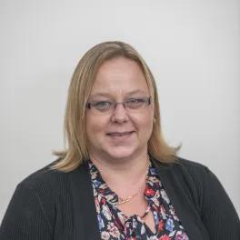 Headshot of a smiling woman wearing a floral blouse, black cardigan and glasses.