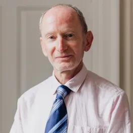 Man in pink top and blue tie looking to camera